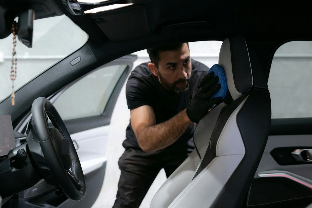 Een man met handschoenen reinigt de bestuurdersstoel van een wagen met de deur open