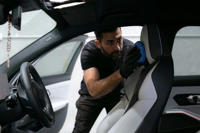 Een man met handschoenen reinigt de bestuurdersstoel van een wagen