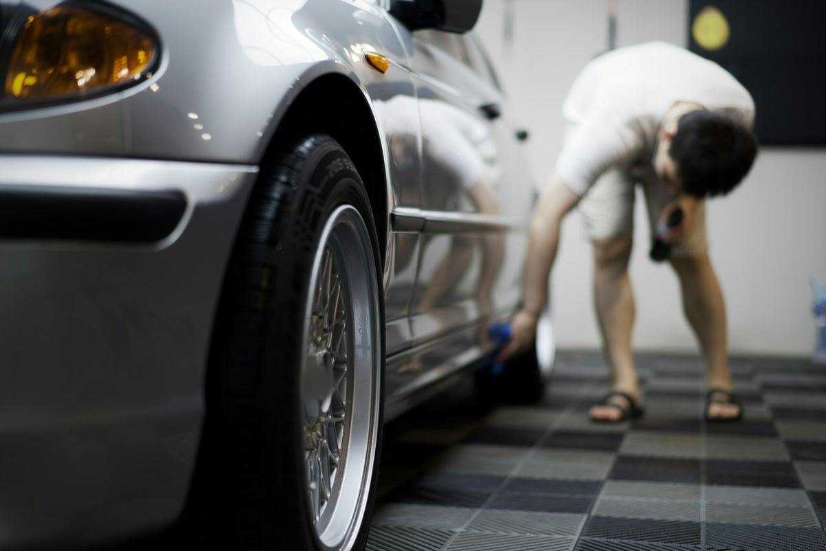 Een man poetst de velg van een zilvergrijze wagen in een werkplaats met een geblokte vloer